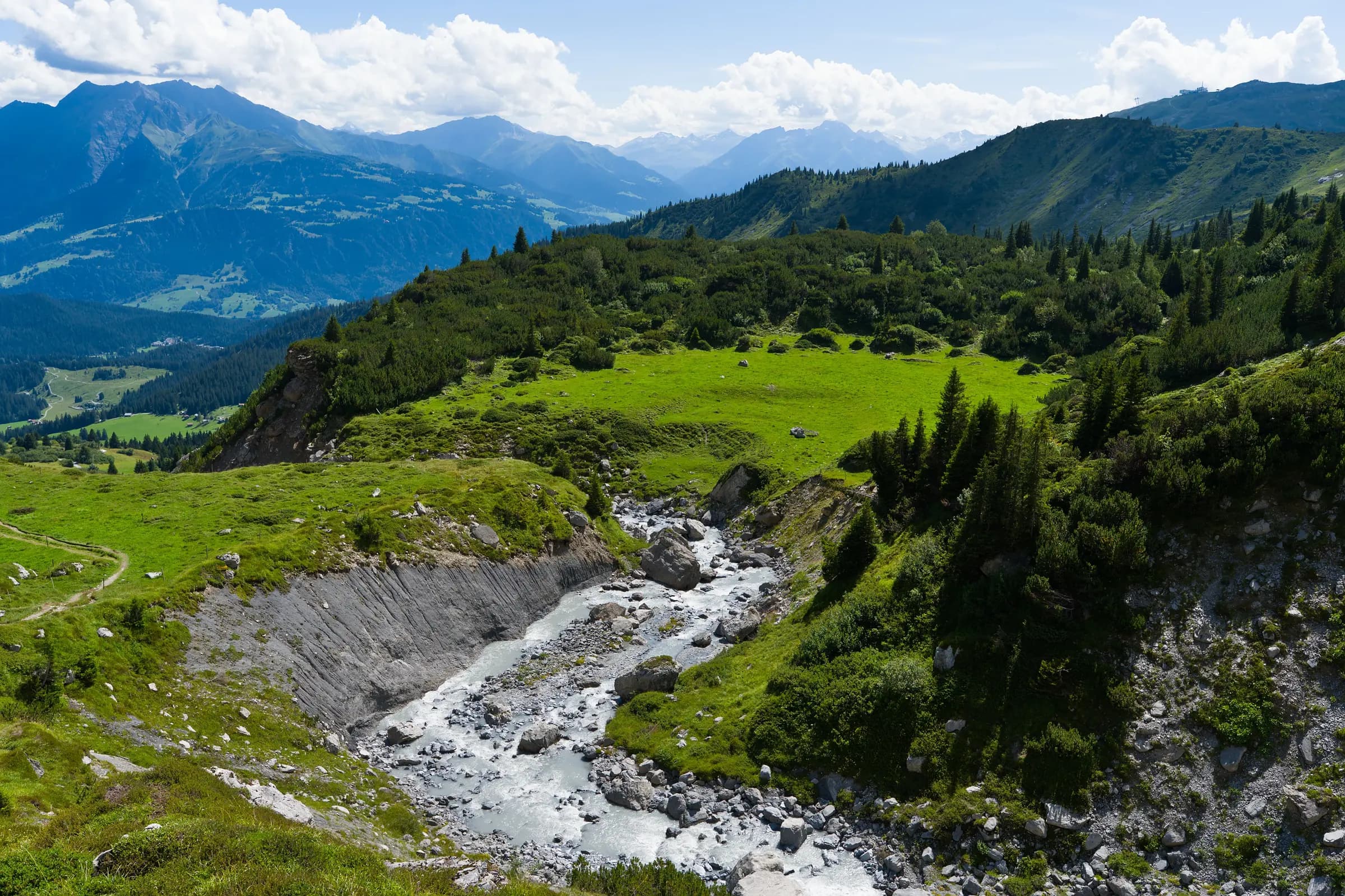 Captivating view of the Swiss Alps with lush greenery and a flowing stream, perfect for nature enthusiasts.