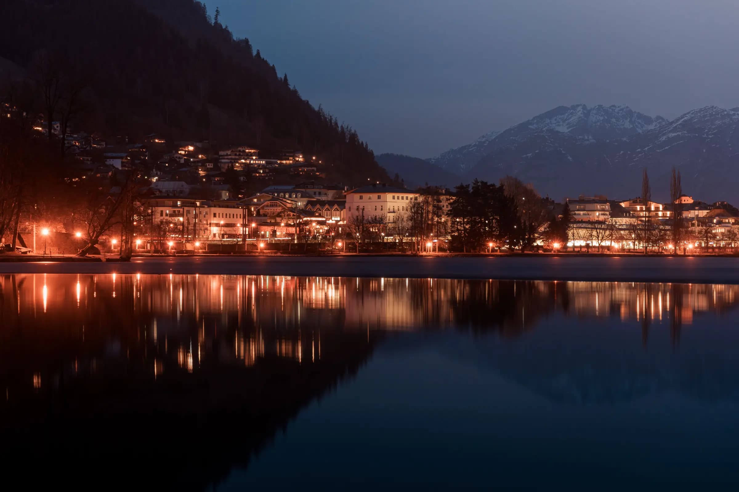 Scenic view of Zell am See town illuminated at dusk, reflecting beautifully in the calm lake waters.