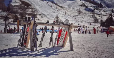 Snowy ski resort with slopes, skis, and snowboards under the bright winter sun.
