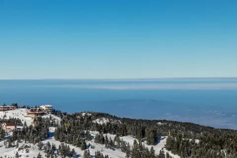 Aerial view of a snow-covered mountain with a ski resort and clear skies.