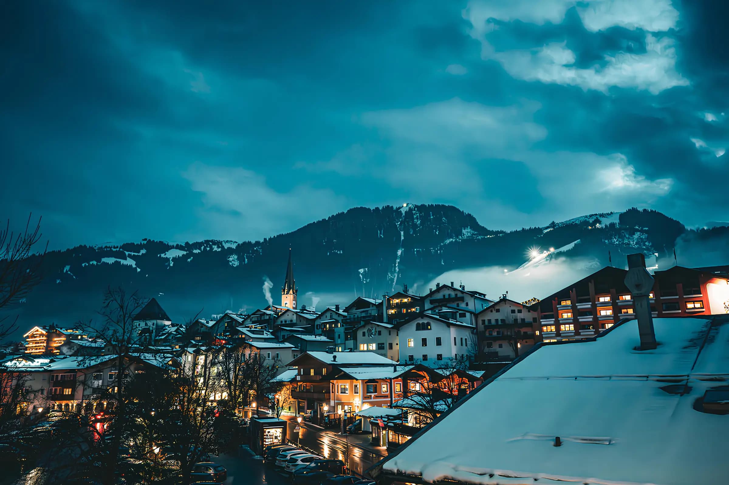 A serene winter evening view of Kitzbühel with snow-capped buildings and mountains.