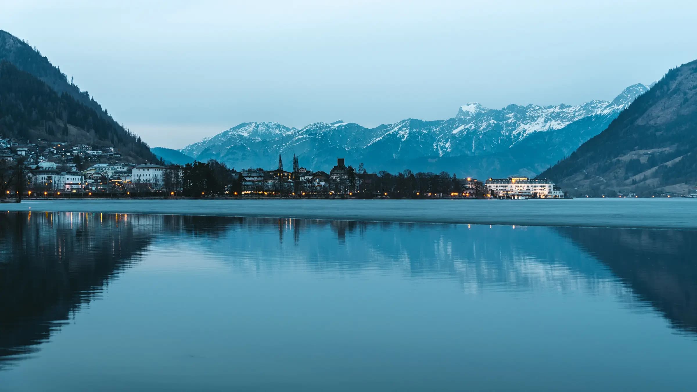 Captivating view of Zell am See with mountains reflecting on a tranquil lake at twilight.
