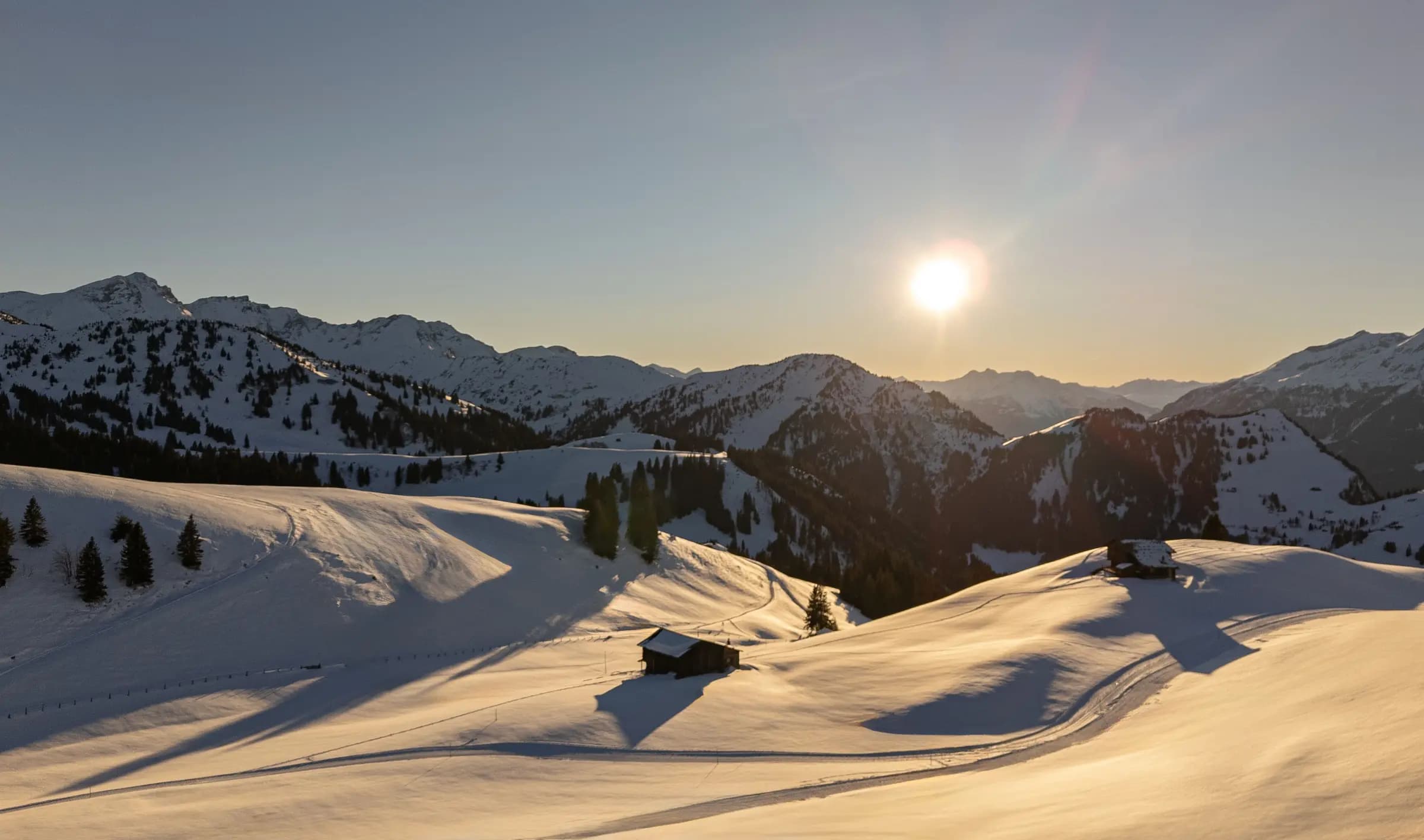 Captivating sunset over snow-covered slopes and wooden barns in Graubünden, Switzerland.