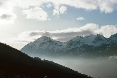 Stunning winter view of snow-covered mountains under a cloudy blue sky, perfect for outdoor enthusiasts.