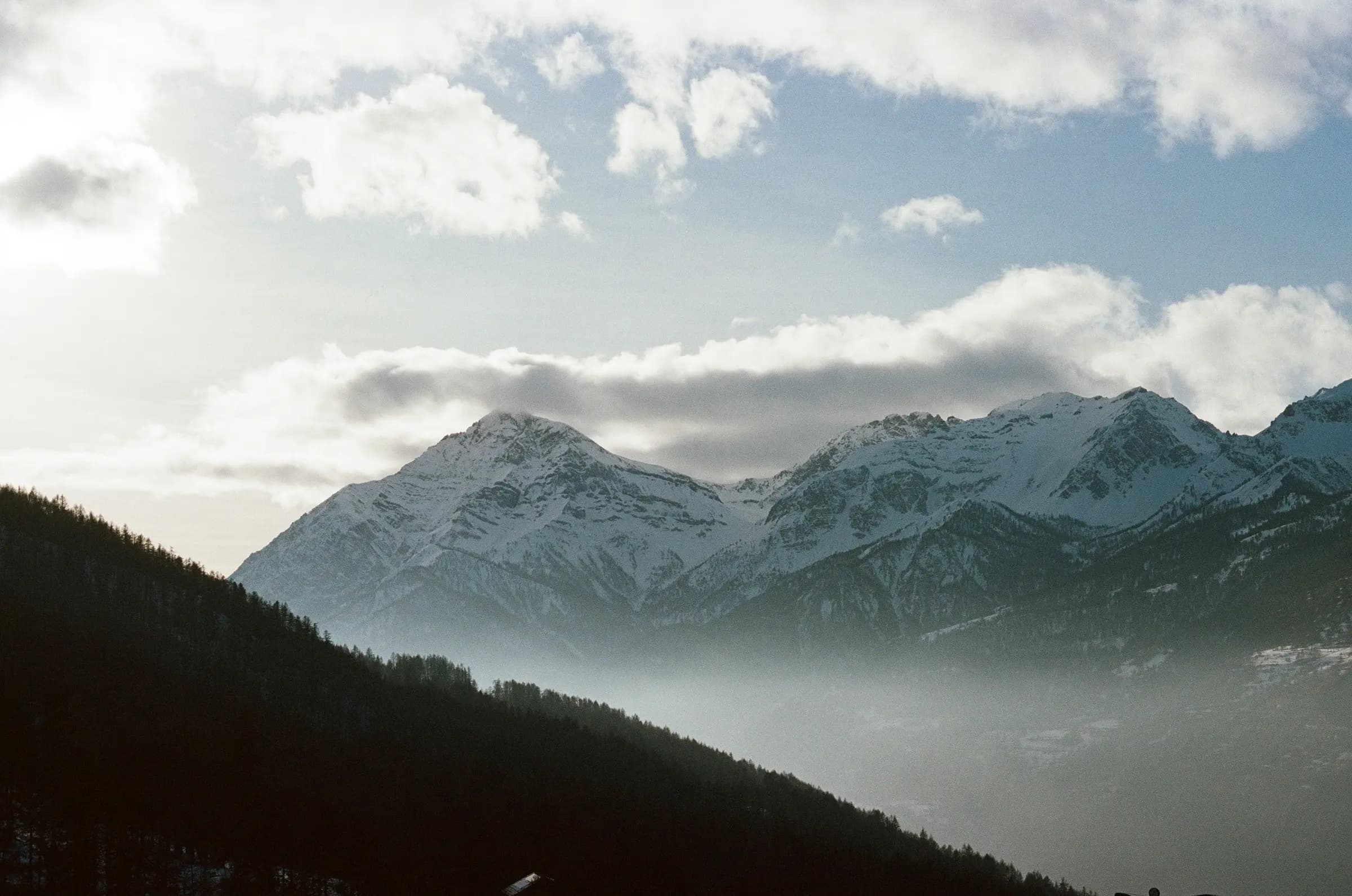 Stunning winter view of snow-covered mountains under a cloudy blue sky, perfect for outdoor enthusiasts.