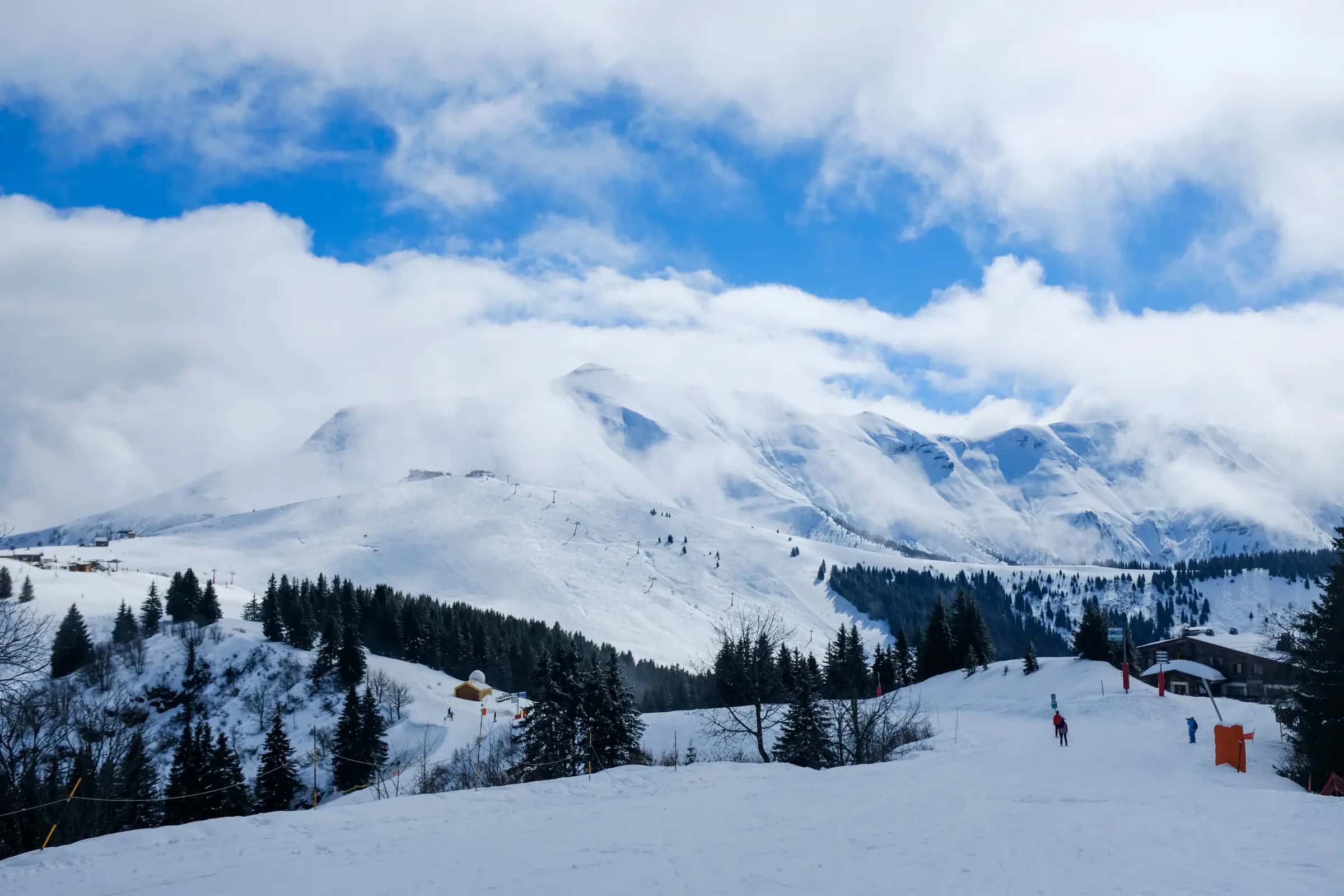 Beautiful winter mountain scene with skiers, trees, and snow-covered peaks.