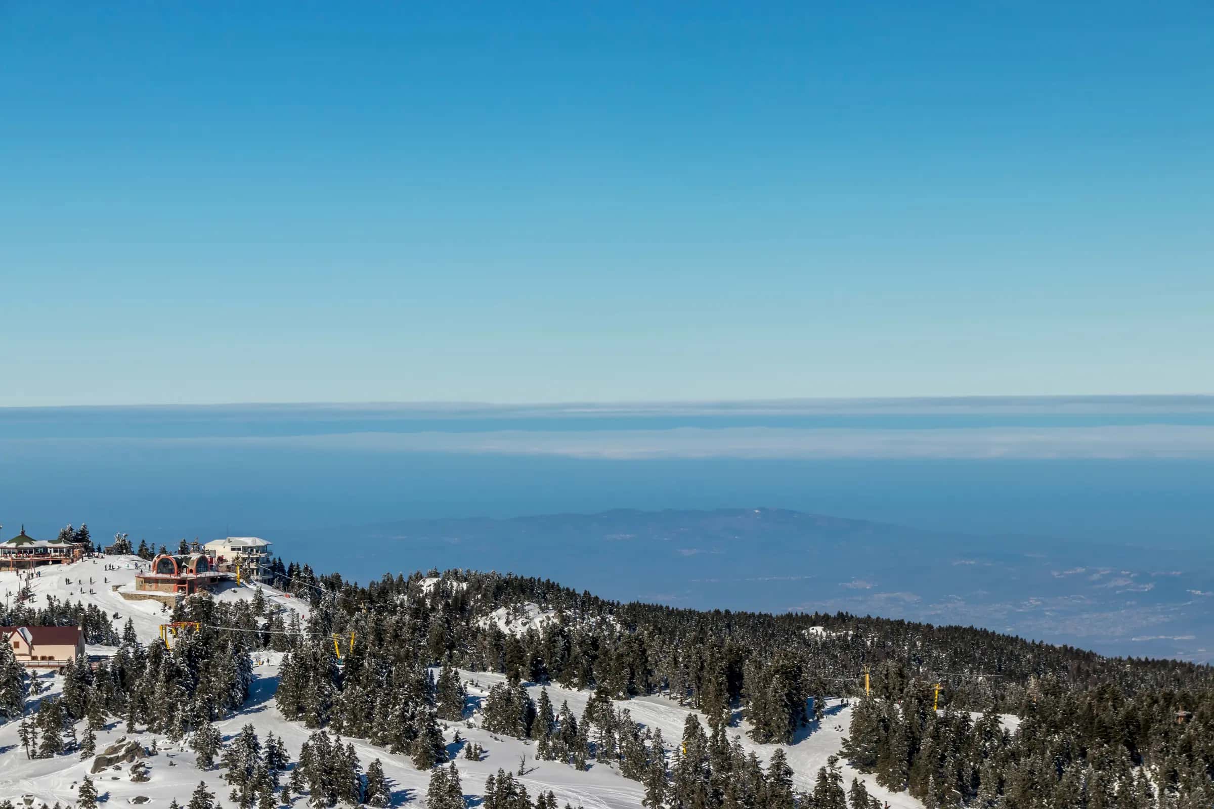 Aerial view of a snow-covered mountain with a ski resort and clear skies.