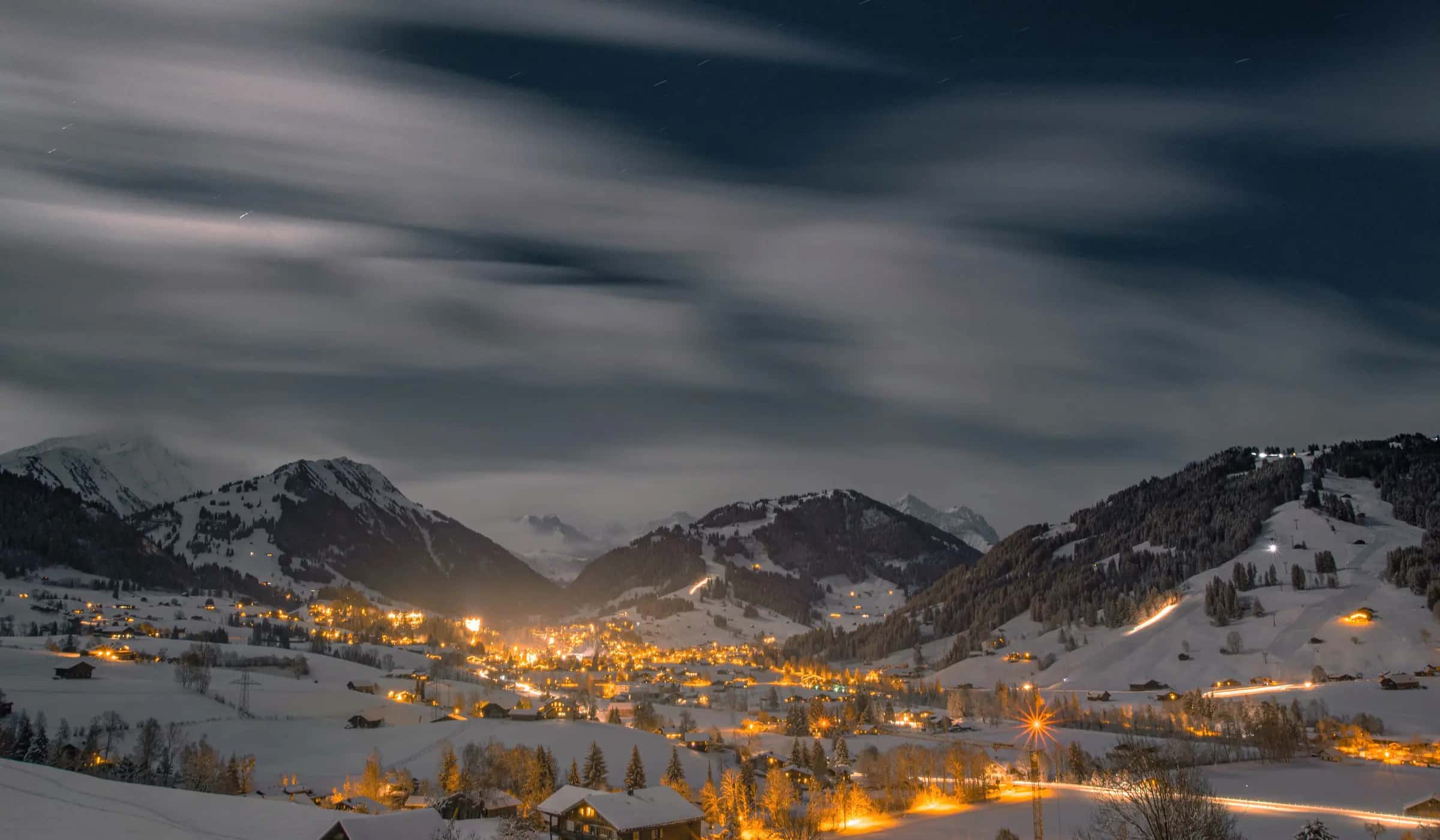 A serene winter night scene of a snowy mountain village illuminated by warm lights under a starry sky.