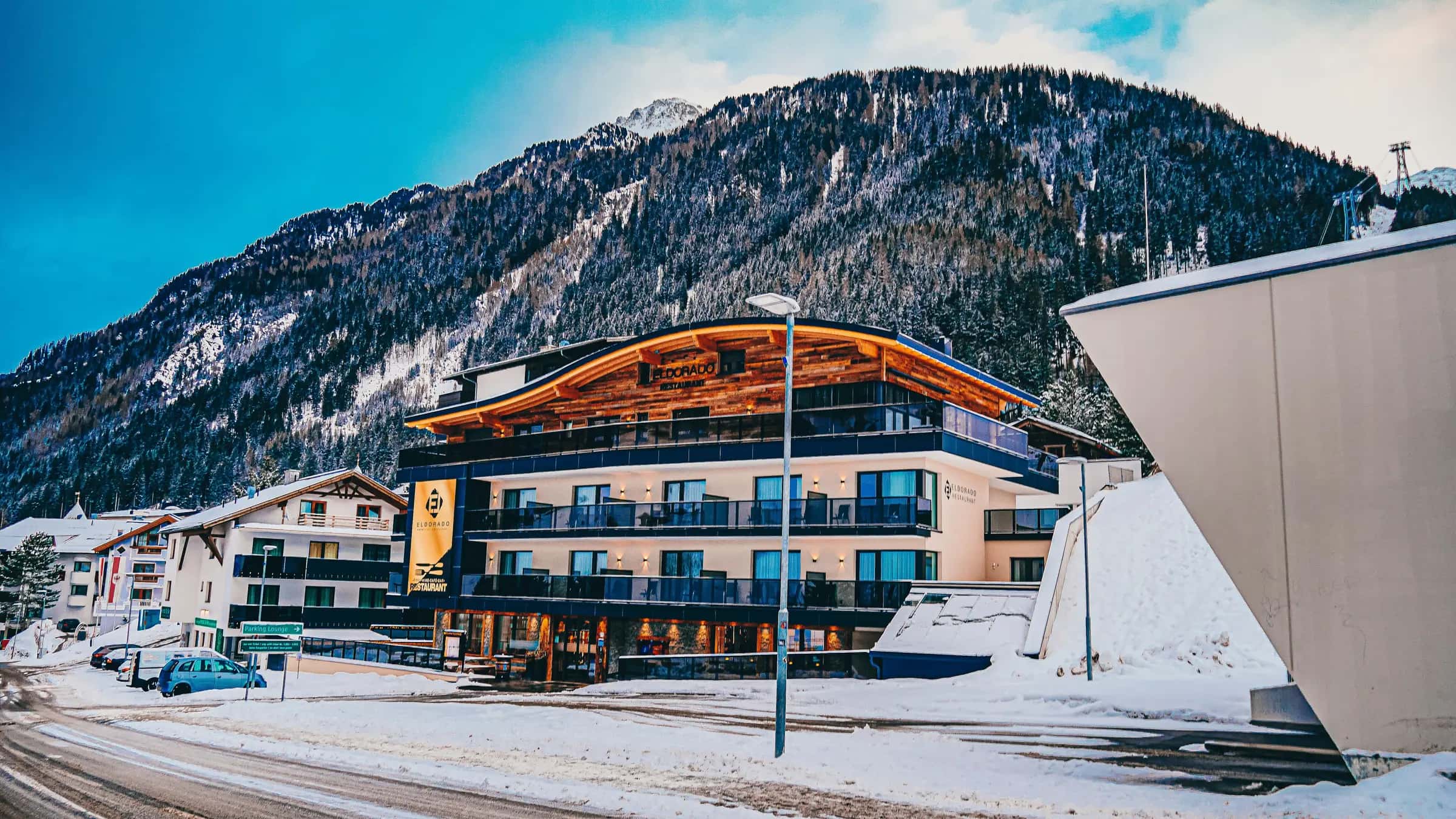 Empty road in front of modern ski resort cottage near snowy mountains on sunny winter day